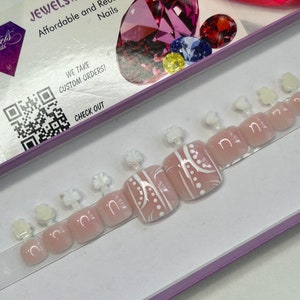 May include: A set of ten pink and white toe nail wraps with a white geometric design. The wraps are displayed in a white box with a purple border. The box also has a QR code and the text "WE TAKE CUSTOM ORDERS!" and "CHECK OUT".