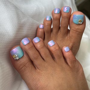 Könnte beinhalten: Nahaufnahme von Füßen einer Person mit blauem und violettem Ombre-Nagellack. Der große Zeh am rechten Fuß hat einen kleinen goldenen Muschelakzent.