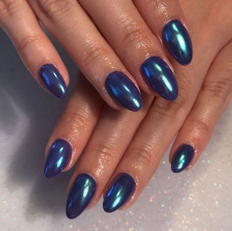 May include: Close-up of hands with oval-shaped nails painted in a dark blue iridescent nail polish.