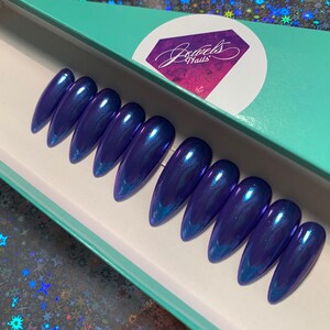 May include: A set of ten blue iridescent stiletto false nails in a teal box with the text "Jewels Nails".