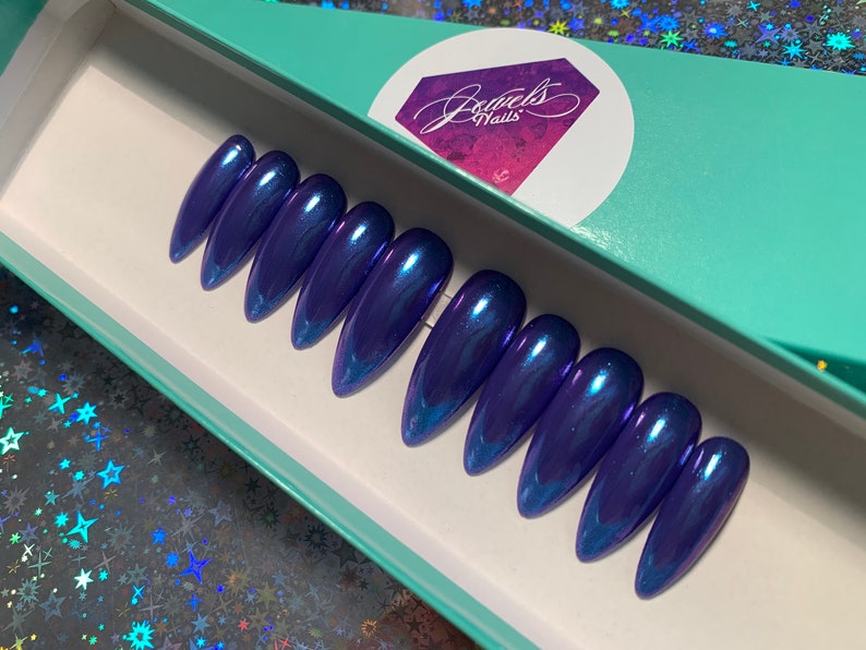 May include: A set of ten blue iridescent stiletto false nails in a teal box with the text "Jewels Nails".