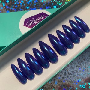 May include: A set of ten long, pointed, blue, iridescent, press-on nails in a teal box with the text "Jewels Nails".