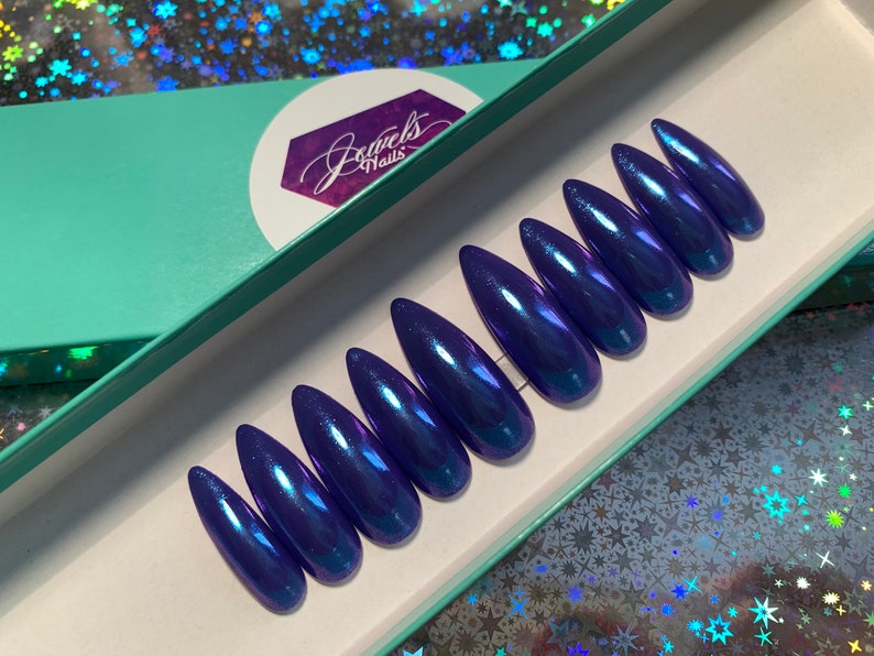 May include: A set of ten long, pointed, blue, iridescent, press-on nails in a teal box with the text "Jewels Nails".
