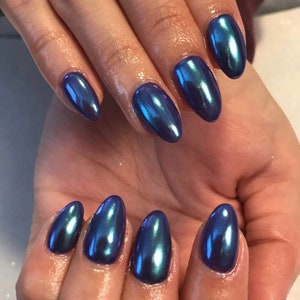 May include: Close-up of a hand with almond-shaped nails painted with a dark blue iridescent nail polish.