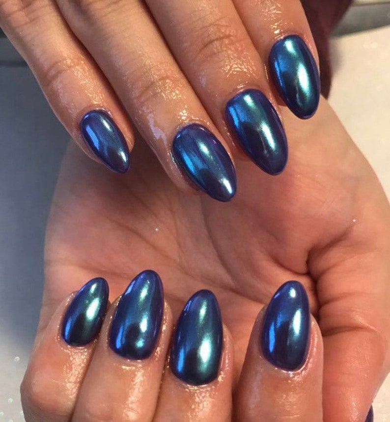 May include: Close-up of a hand with almond-shaped nails painted with a dark blue iridescent nail polish.