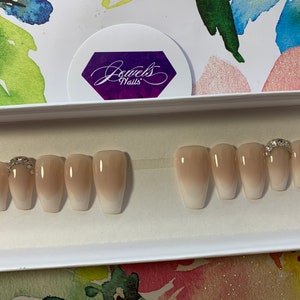 May include: A set of ten nude ombre coffin-shaped press-on nails with a single rhinestone accent on the ring finger.