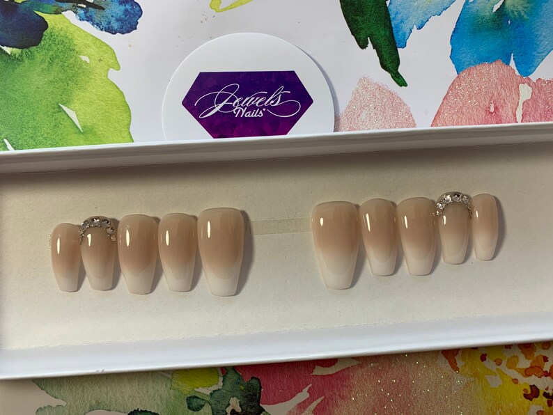 May include: A set of ten nude ombre coffin-shaped press-on nails with a single rhinestone accent on the ring finger.