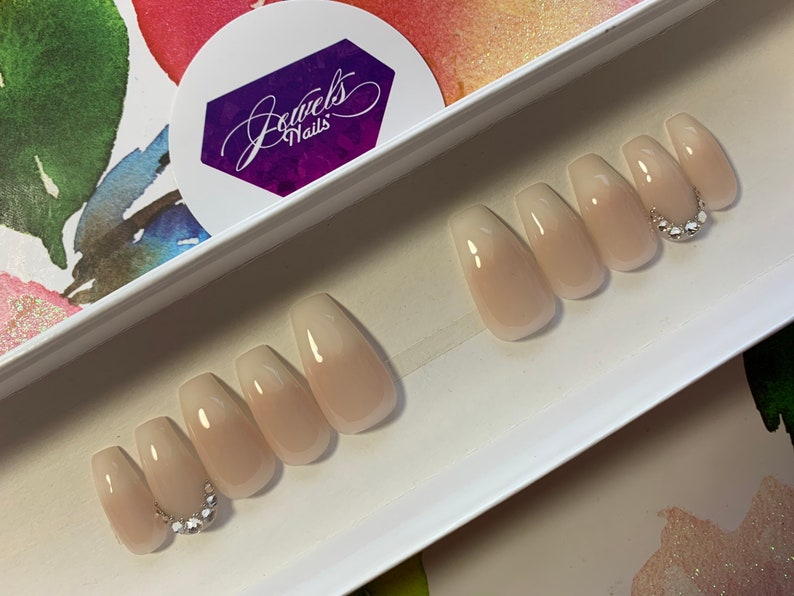 May include: Set of ten nude ombre coffin-shaped press-on nails with a single row of rhinestones on one nail. The nails are displayed in a white box with the text "Jewels Nails" on a purple sticker.