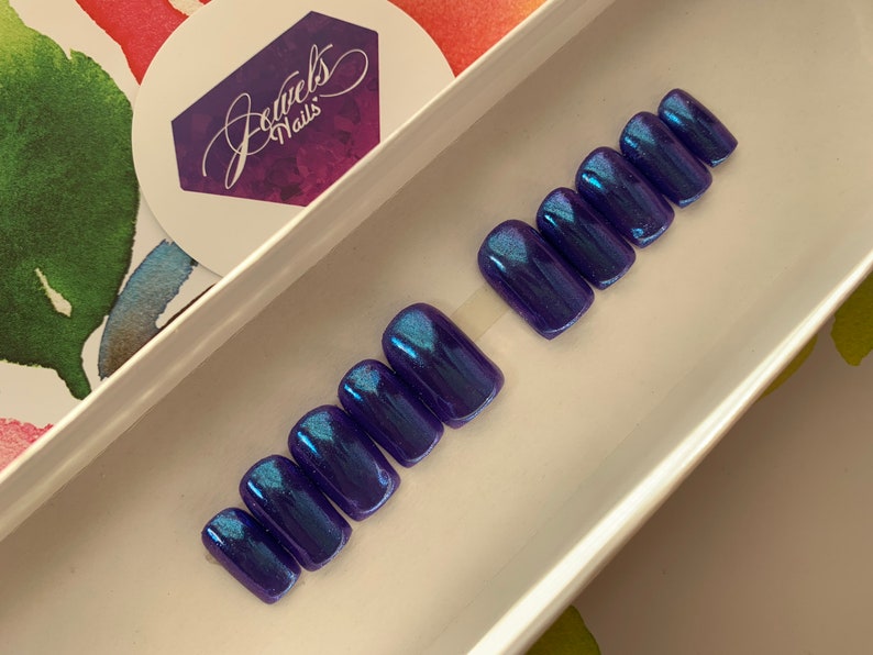 May include: Set of ten blue and purple iridescent press-on nails in a square shape.