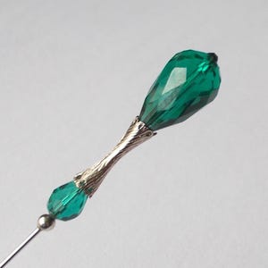 May include: A silver and emerald green glass pin with a teardrop-shaped crystal on top.