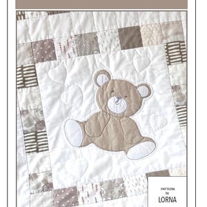 Peut inclure: Un patron de courtepointe patchwork intitulé "Honey and Hugs" avec un appliqué d'ours en peluche. La courtepointe a un design carré, mesurant 101,6 cm x 101,6 cm une fois terminée. L'ours est brun clair avec des accents blancs, entouré de cœurs.