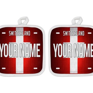 May include: Two red and white pot holders with the Swiss flag and the text "Switzerland" and "Your Name" printed on them.