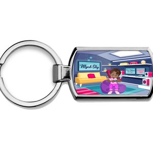 May include: A silver keyring with a rectangular tag featuring a cartoon illustration of a young girl playing video games in her bedroom. The tag has the text "Myah Sky" on it.