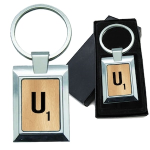 May include: A silver metal keychain with a wooden tile featuring the letter "U" and the number "1" in black text. The keychain is in a black box.