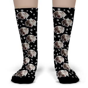 May include: Black knee-high socks featuring a repeating pattern of Weimaraner dog faces, white paw prints, and bone shapes. The socks are designed to be worn on the legs and feet.