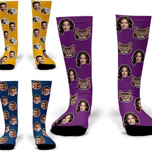 May include: A collection of knee-high socks in various colors, each featuring a repeating pattern of faces, cats, and dogs. The socks are yellow, purple, and blue, with black accents at the toes and heels.