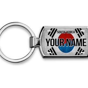 Puede incluir: Un llavero plateado con una etiqueta rectangular que muestra la bandera de Corea del Sur y el texto "SOUTH KOREA" y "YOUR NAME".