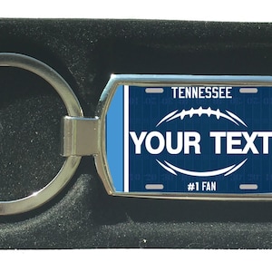 Könnte beinhalten: Ein silberner Schlüsselanhänger mit einem blauen und weißen Tennessee-Kennzeichen-Design. Das Kennzeichen hat eine Fußballgrafik und den Text "YOUR TEXT #1 FAN".