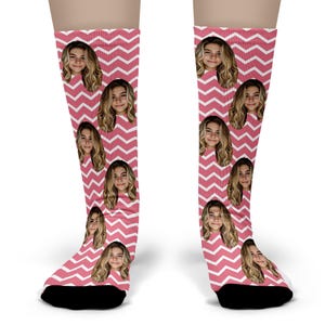 May include: A pair of knee-high socks featuring a repeating pattern of a person's face and a pink and white chevron design. The socks have black heels and toes.