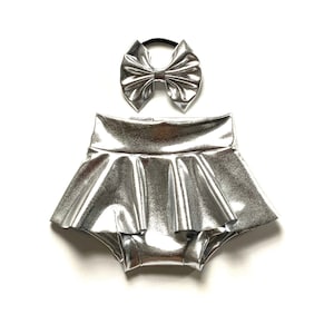 May include: Silver metallic ruffled shorts with a matching silver bow headband.