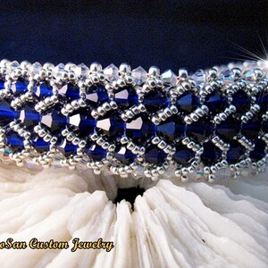 May include: A close-up of a beaded bracelet with dark blue crystals and silver beads. The bracelet is presented on a white, textured surface. The jewelry is labelled "Rosan Custom Jewelry".