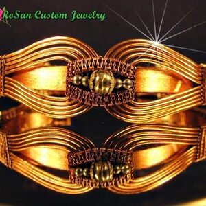 May include: A gold-toned wire-wrapped bracelet with a central decorative element featuring a round, textured bead. The bracelet is made of multiple strands of wire, creating a layered and intricate design.