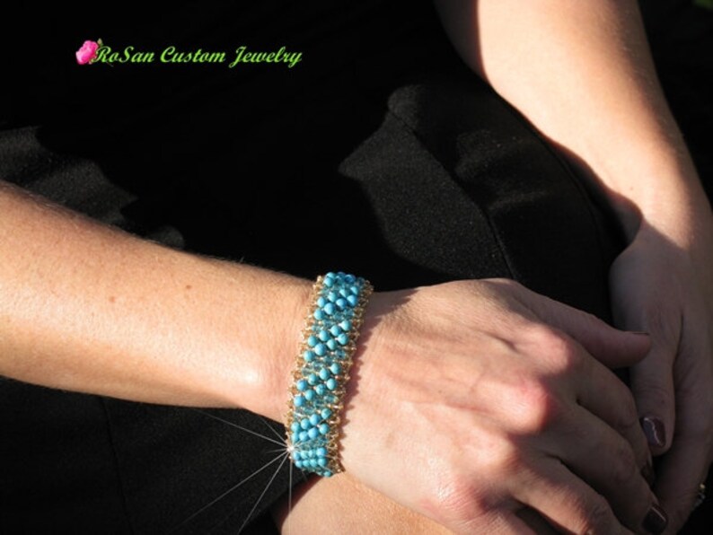 May include: A turquoise and gold beaded bracelet with a woven design. The bracelet is on a person's wrist.