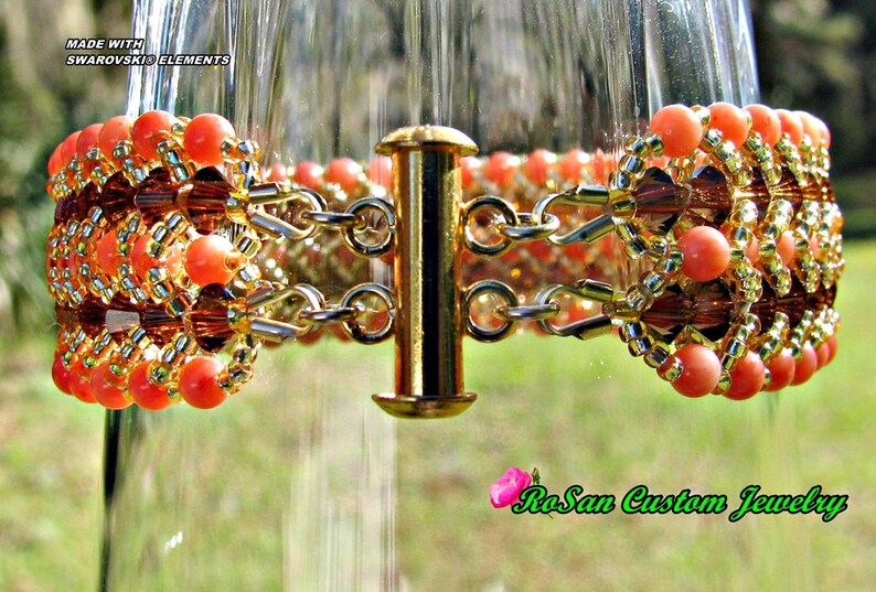 May include: A gold chain bracelet with orange and brown beads. The bracelet is made with Swarovski elements and has a clasp closure. The bracelet is displayed on a glass surface.