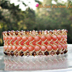 May include: A delicate bracelet with a woven design featuring pink and brown beads. The bracelet is made with small, round beads and has a subtle shimmer.
