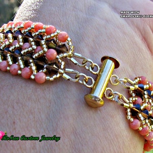 May include: A multi-strand bracelet with pink, gold, and black beads. The bracelet has a gold toggle clasp and is made with Swarovski elements. The bracelet is on a person's wrist. "RoSan Custom Jewelry" is written on the bracelet.