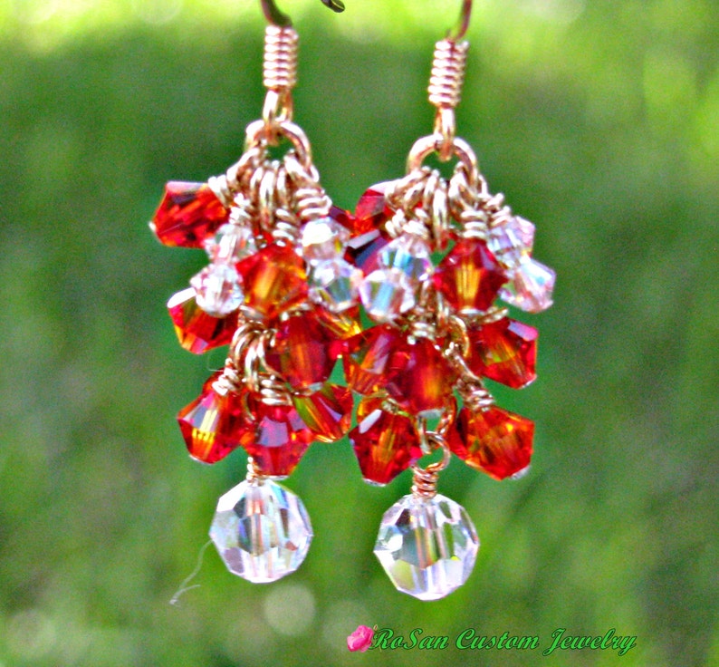 May include: Gold dangle earrings with red and clear crystal beads. The earrings are made with wire wrapped beads and have a teardrop shape.
