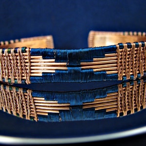 May include: A copper wire bracelet with a woven design and blue accents. The bracelet is made of copper wire and is woven with a blue thread.