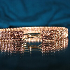 May include: A copper wire bracelet with a woven design and a clasp. The bracelet is made of multiple strands of copper wire that are woven together to create a intricate pattern. The clasp is made of a single strand of copper wire that is twisted into a loop.