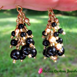 May include: Gold dangle earrings with black and gold beads. The earrings are made with multiple layers of beads and have a tassel-like appearance.