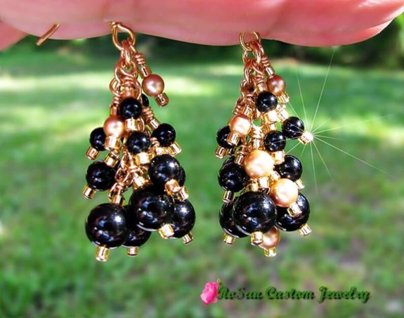 May include: Gold dangle earrings with black and gold beads. The earrings are made with multiple layers of beads and have a tassel-like appearance.