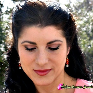 May include: A woman with long dark hair wearing red and white earrings. She is looking down with her eyes closed. The text "RoSan Custom Jewelry" is visible in the bottom right corner of the image.