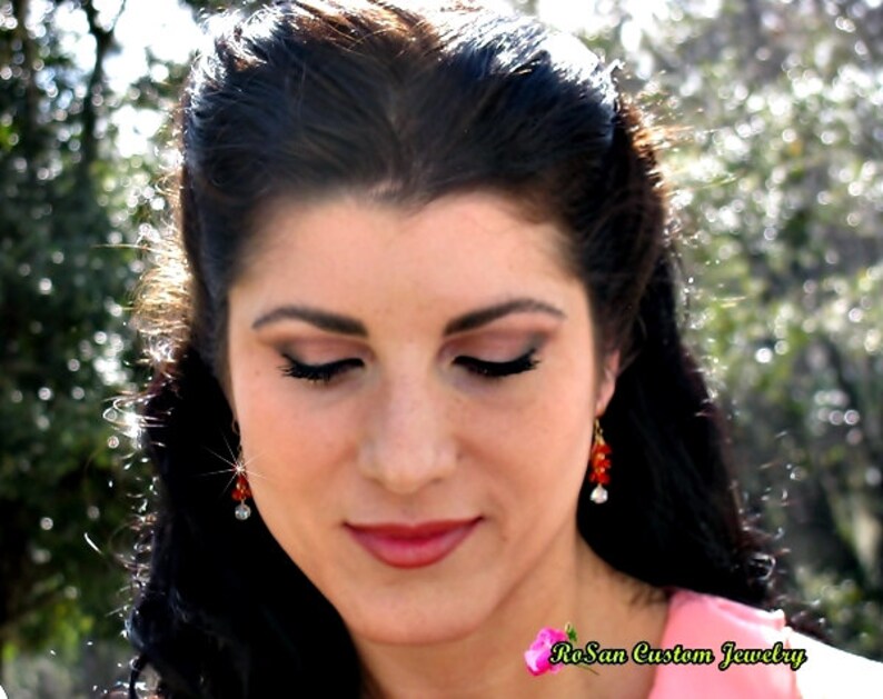 May include: A woman with long dark hair wearing red and white earrings. She is looking down with her eyes closed. The text "RoSan Custom Jewelry" is visible in the bottom right corner of the image.