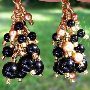 May include: Gold tone dangle earrings with black and gold beads. The earrings are made with a cluster of black beads and gold beads.