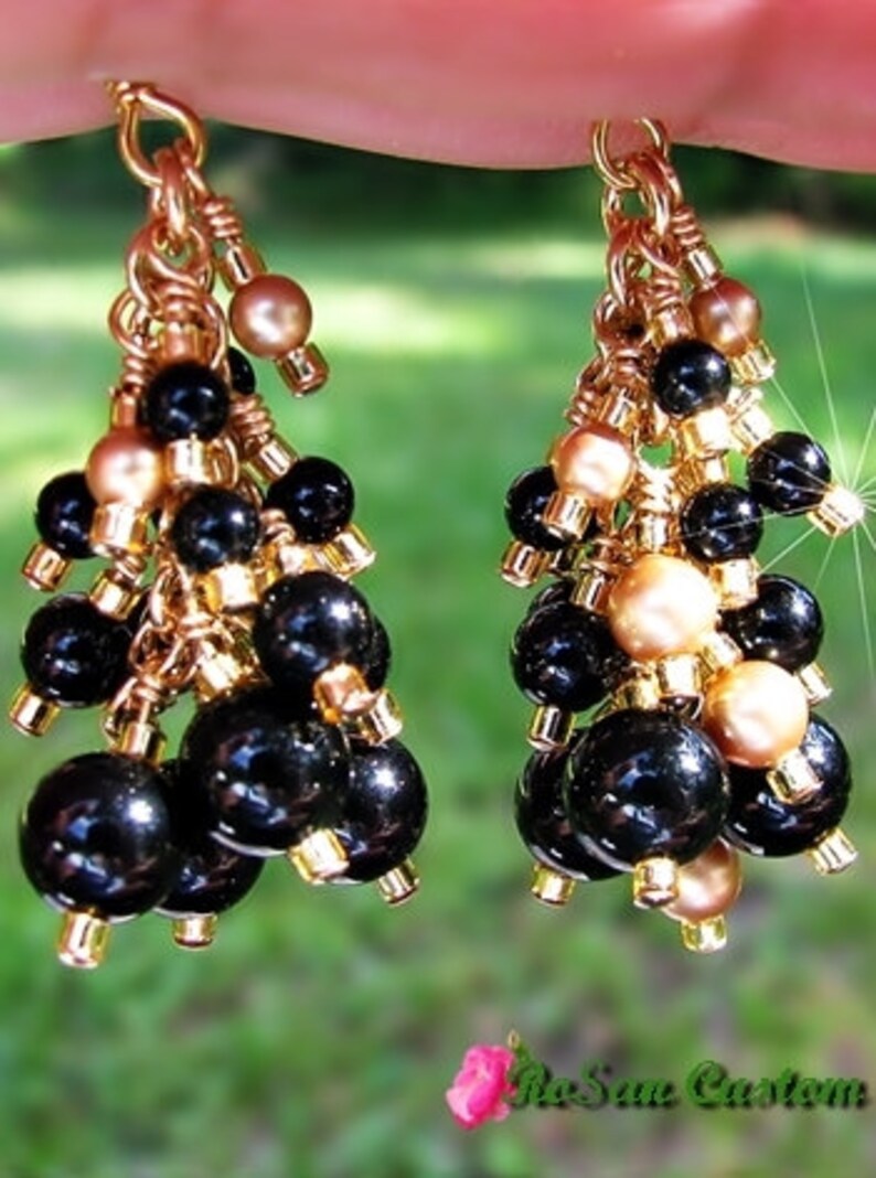 May include: Gold tone dangle earrings with black and gold beads. The earrings are made with a cluster of black beads and gold beads.