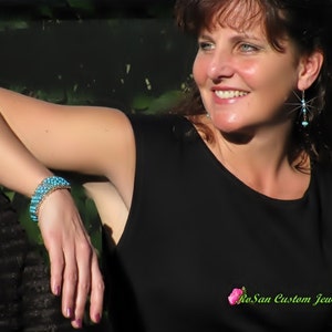 May include: A woman wearing a black top and turquoise earrings with a turquoise beaded bracelet on her wrist. The text "RoSan Custom Jewelry" is visible in the bottom right corner of the image.