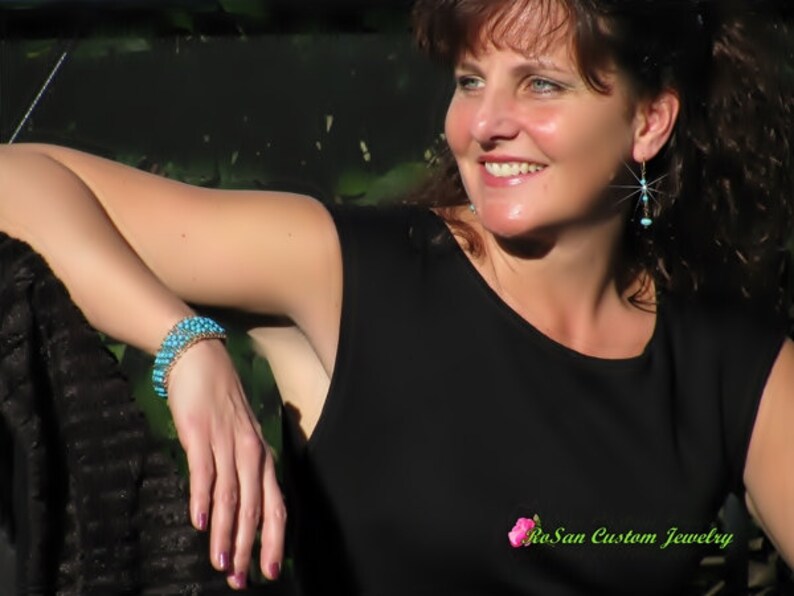 May include: A woman wearing a black top and turquoise earrings with a turquoise beaded bracelet on her wrist. The text "RoSan Custom Jewelry" is visible in the bottom right corner of the image.