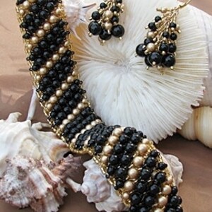 May include: A black and gold beaded bracelet and matching earrings. The bracelet is made with small black and gold beads woven together in a pattern. The earrings are dangle earrings with multiple tiers of black and gold beads.