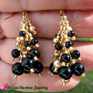 May include: Gold tone earrings with black and gold beads. The earrings are dangling and have a tassel-like design.