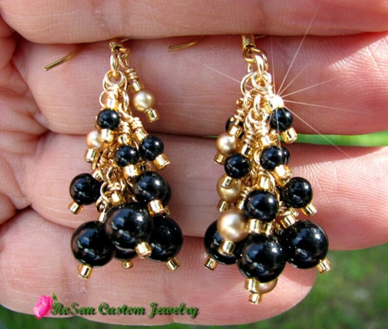 May include: Gold tone earrings with black and gold beads. The earrings are dangling and have a tassel-like design.