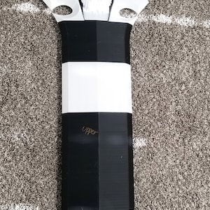 Puede incluir: Una espada de utilería negra y blanca con un diseño de calavera en la parte superior. La espada mide 1,37 metros de largo.