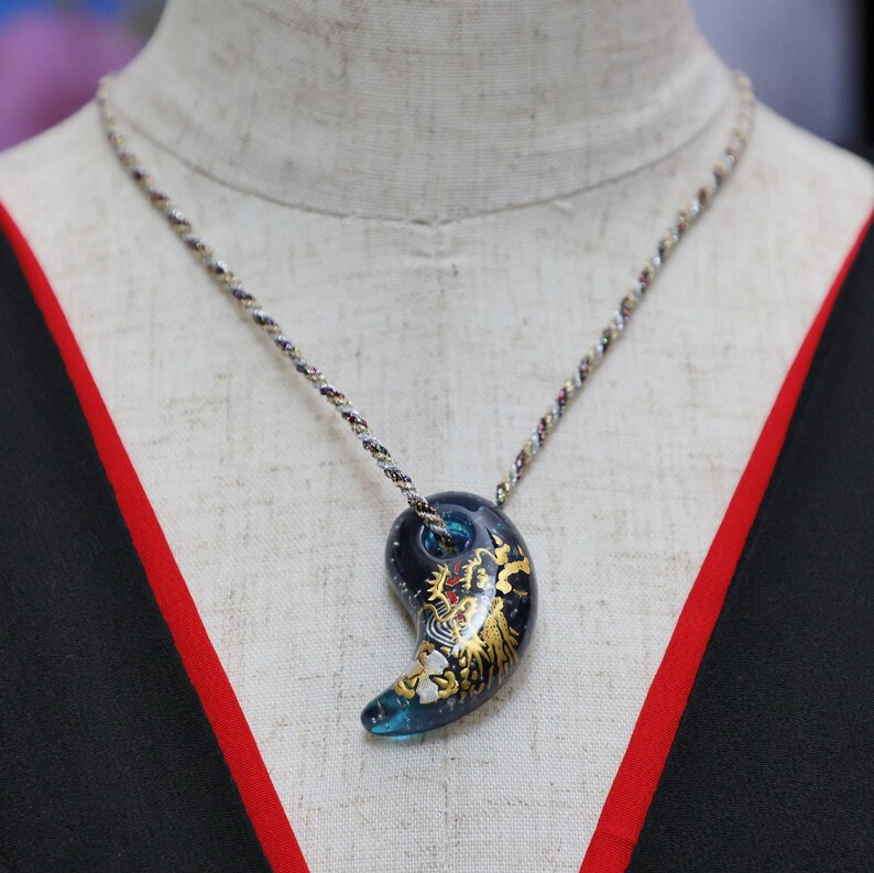 May include: A blue and gold pendant necklace with a yin yang design. The pendant features a dragon and floral details.