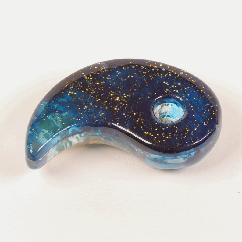 May include: A blue and gold glass pipe shaped like a yin yang symbol. The pipe has a small hole in the center for smoking.