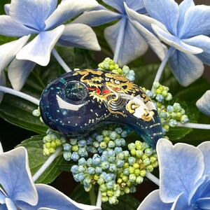 May include: A blue glass pendant with a gold and white dragon design. The pendant is shaped like a crescent moon and has a small hole at the top for hanging.