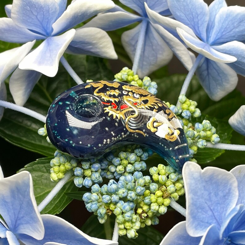 May include: A blue glass pendant with a gold and white dragon design. The pendant is shaped like a crescent moon and has a small hole at the top for hanging.