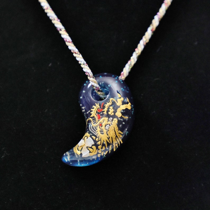 May include: A blue and gold pendant necklace with a dragon design. The pendant is shaped like a crescent moon and has a white cord.